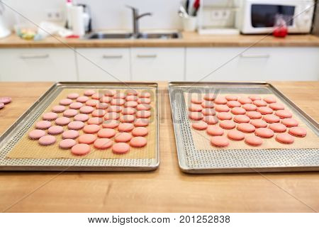 cooking, confectionery and baking concept - macarons on oven trays at bakery or pastry shop kitchen