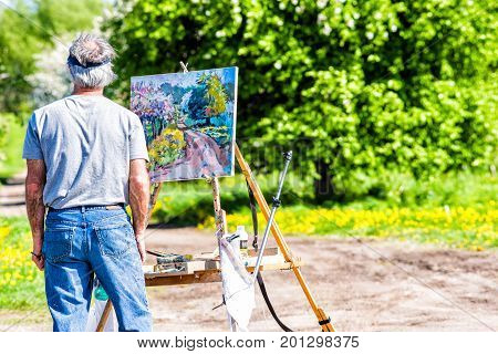 Ile D'Orleans Canada - June 1 2017: Artist man with painting on easel by countryside landscape in summer and trail path road with flowers