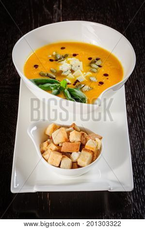 Pumpkin soup with cream and pumpkin seeds on dark wooden background. Copy space.