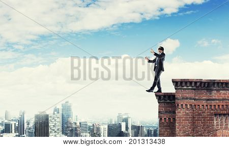 Businessman with blindfolder on eyes walking on building top