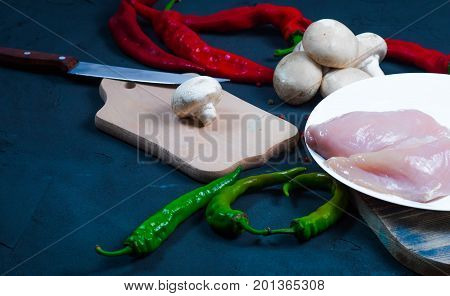 raw chicken wings with herbs in a transparent bowl Cauliflower with tomatoes and herbs and hot peppers with mushrooms on wooden background top view close up.
