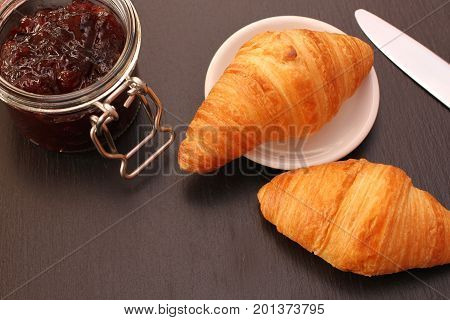 French Croissant with jam jar and knife on black background