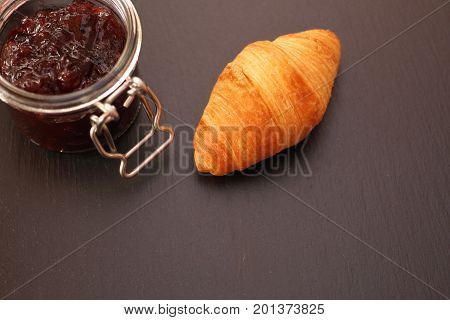 French Croissant with jam jar on black background