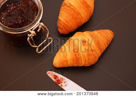 French Croissant with jam jar an knife on black background