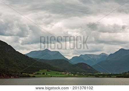 Little village and mountains along the Romsdalsfjorden near Andalsnes under a cloudy sky Norway
