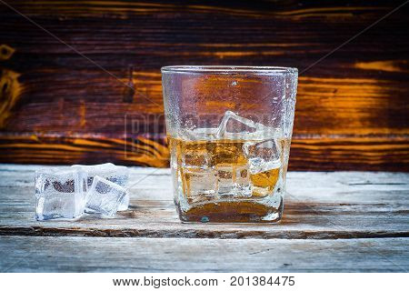Two glasses of whiskey with ice cubes served on wooden planks. Vintage countertop with highlight and a glass of hard liquor