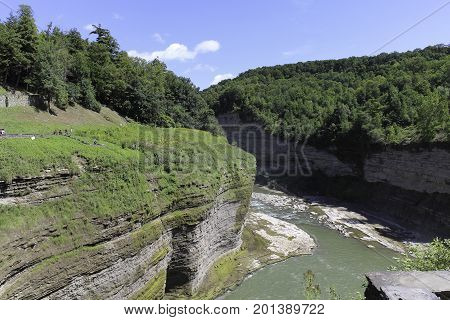 Genesee river flowing through the Letchworth State Park gorge. Steep walls of the gorge. Forest and trees on banks of the gorge. Blue skies and white clouds.