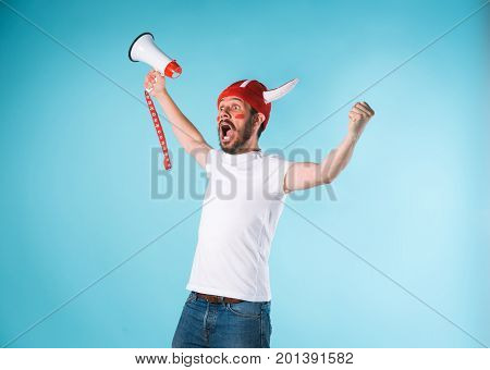 The football fan with megaphone over blue. The young man looking at camera with different emotions on face