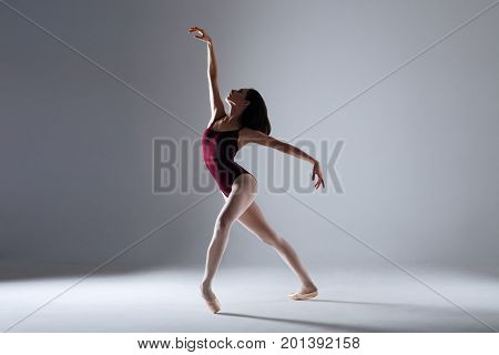 Slim ballerina is dancing in the white studio in the contrast light