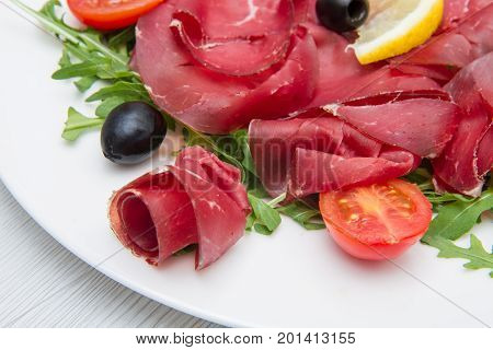 a dish of bresaola and aragula and black olives