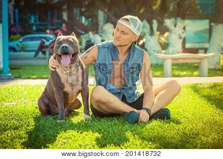 Man and dog american pit bull terrier relaxing at the park embracing and hugging. Caucasian male with strong dog