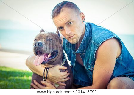 Man and dog american pit bull terrier relaxing at the park embracing and hugging. Caucasian male with strong dog