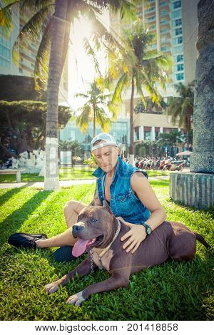 Man and dog american pit bull terrier relaxing at the park embracing and hugging. Caucasian male with strong dog