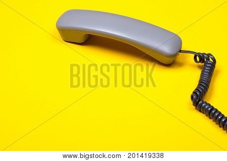 Top view of gray telephone handset. receiver and cord on yellow background.