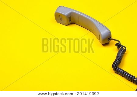 Top view of gray telephone handset. receiver and cord on yellow background.