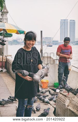 Bangkok, Thailand - January 8, 2016: Thai girl and boy smiling and feeding pigeons on the waterfront of Wat Rakhang Pier, Bangkok, Thailand. Here is the famous Wat Rakhang Girls' School.