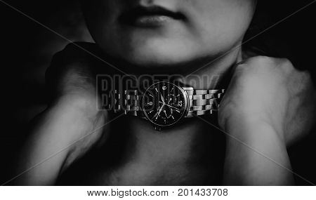 women hands clasp the neck of the watch in an attempt to break the time that suffocates, the part of the chin is visible, two hands are clenched into fists, the iron strap of the clock around the neck