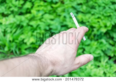 The hand holds a cigarette against the background of green grass.