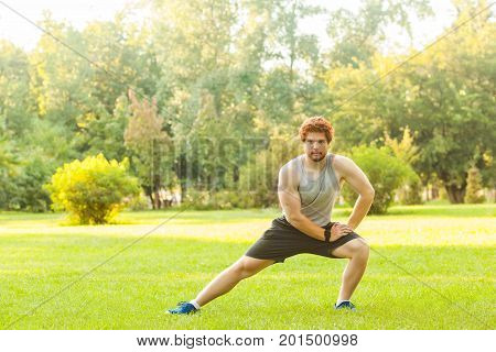 Workout in summer morning. Muscules redhead athlete doing gymnastic and looking at camera