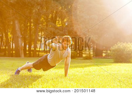 Hello! Training in one summer morning. Young adult bearded man looking in camera and doing exercise. Outdoor