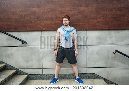 Young adult athlete stay ahead of gray wall looking at camera seriosly