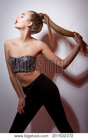 beautiful young woman with ponytail hairstyle and red lips  dressed in sparkling bra and black jeans. copy space.