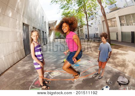 Kids jump over elastic rope smiling and happy with curly African girl in the air