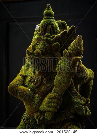 Balinese Carved Stone Statue of Rakasa covered with green moss. at Hindu Temple.
