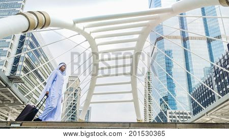 Business arab traveler man carrying a suitcase and walk in the business landmark city with the modern steel structure and exterior wall modern building