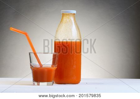 A bottle of carrot juice and a glass of carrot juice with a straw on white wood table. Still life of a healthy eating concept