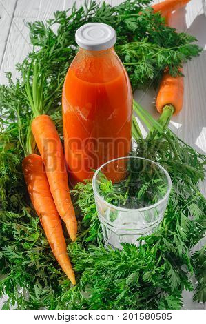 A bottle of carrot juice with empty glass and some fresh carrots on white wood table. Still life of a healthy eating concept