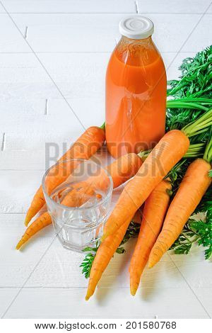 A bottle of carrot juice with empty glass and some fresh carrots on white wood table. Still life of a healthy eating concept