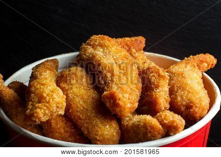 Bucket of chicken nagets. It stands on the black slate, side view.