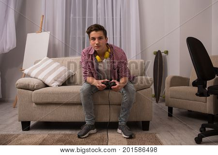 Teenage boy sitting on sofa playing computer games. Young boy at home, concerned with computer games.
