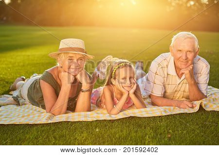Happy grandparents with grandchild. People lying outdoors summer.
