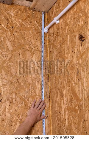 Plumber installing pipes in home measurement of distance on a wooden wall using a measuring tape wall mounting of a plastic water pipe.