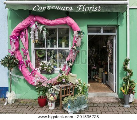 Clifden Ireland - August 4 2017: The green facade of the small business Connemara Florist shows plants flowers and a large pink wreath around the window. Open door and street scene.