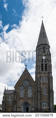 Clifden Ireland - August 4 2017: Portrait of the brown-gray entrance facade and tower of the local Catholic Saint Joseph church against white clouds in blue sky.