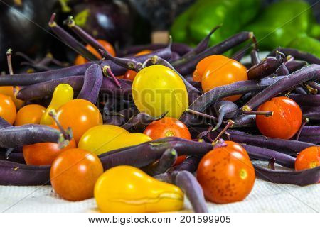 Horizontal photo of colorful tomatoes purple beans bell peppers and eggplant on a white surface