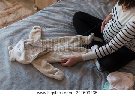Pregnant woman dreaming and holding baby's clothes.