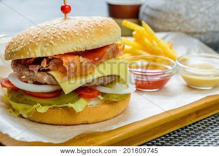 Cheese burger with bakon garnished with sauces and french fries