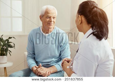 Elderly patient. Nice pleasant aged man looking at his nurse and talking to her while being at the health center