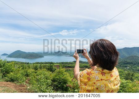 Female traveler with smart phone taking a photo of beautiful landscape at kanchanaburi thailand