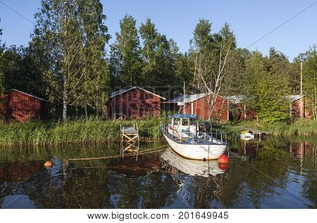 KOKKOLA, FINLAND ON JULY 07. View of a channel, a white boat and red wooden boathouses by the seaside on July 07, 2017 in Kokkola, Finland. Evening and bright sunshine. Editorial use.