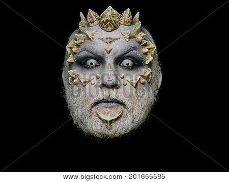 Monster face with scary look of white eyes. Alien or reptilian makeup with sharp thorns and warts. Demon head isolated on black. Horror and fantasy concept. Man with dragon skin and beard.