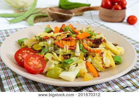 Vegetable stew - a mixture of baked cabbage green beans onions carrots cherry tomatoes sweet pepper on a plate on a white wooden background. Vegan cuisine. Proper nutrition.