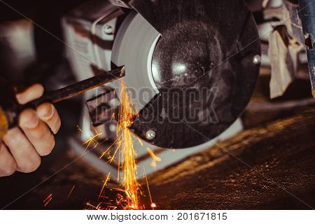 Sharpening a chisel on grinding machine with sparks fly