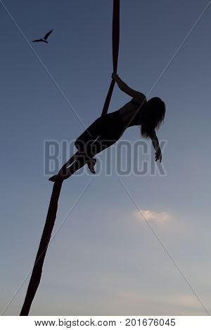 Female gymnast in the air on a hammock shows sporting tricks.