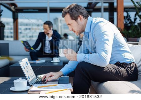 Hard work and persistence. Pleasant nice hard working businessman having coffee and working on a laptop while sitting in the cafe
