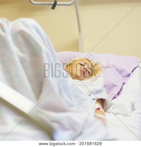 Bedridden female patient lying in hospital bed, recovering after surgery.